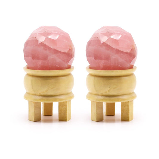 Two faceted rose quartz spheres rest on small, light-colored wooden stands with four legs, displayed against a white background.