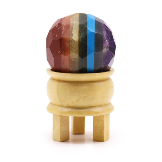 A multi-colored stone sphere rests on a small, light-colored wooden stand against a white background.