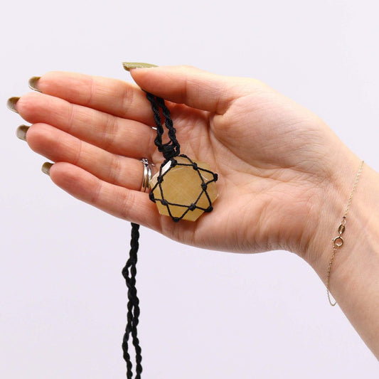 A yellow, star-shaped stone pendant, held by a black, knotted cord, sits on a person's open palm against a white backdrop.