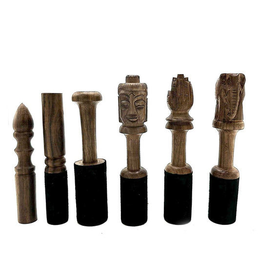 Six wooden mallets, carved with various figures, stand on a white background. The figures include a Buddha, praying hands, and an elephant. Each mallet has a dark cylindrical base.