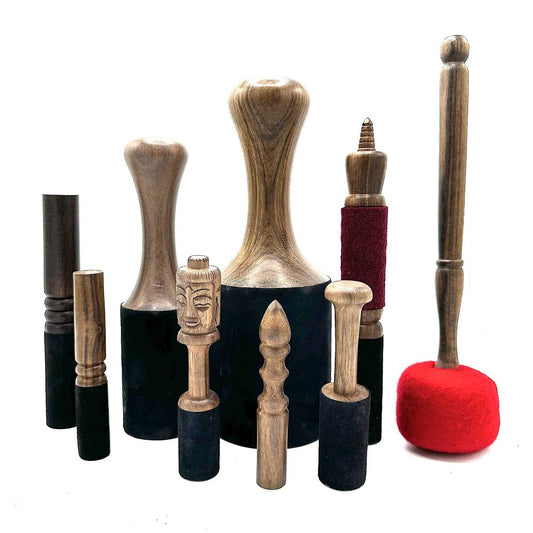Wooden singing bowls and mallets are arranged on a white surface. They vary in size and shape; some have carved faces.