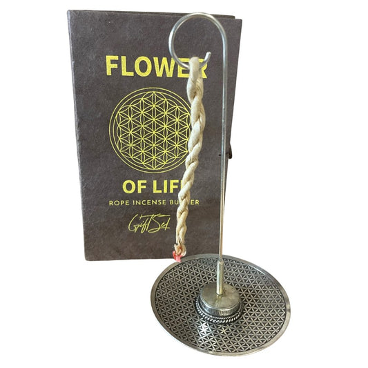 A twisted rope incense burns on a metal stand with a geometric design. Behind it, a box labeled "FLOWER OF LIFE ROPE INCENSE BURNER Gift Set" displays a circular pattern.