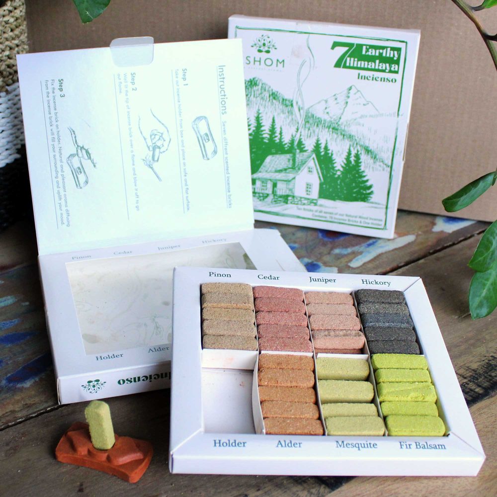 Incense sticks in a box, labeled by fragrance: Pinon, Cedar, Juniper, Hickory, Alder, Mesquite, Fir Balsam. Instructions inside lid. Background features box with green mountain and cabin illustration.