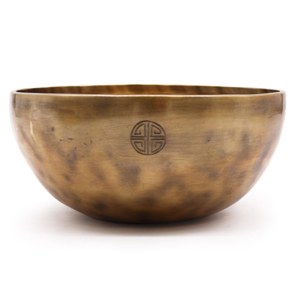 A bronze singing bowl sits still, featuring a circular symbol on its side, against a plain white background.