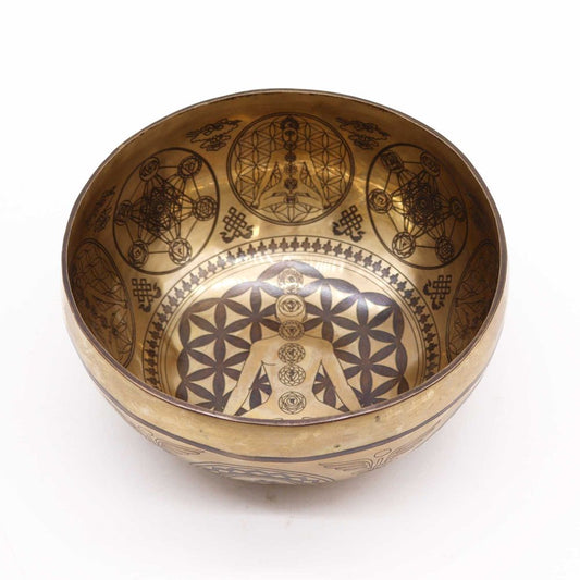 A brass bowl features intricate geometric and spiritual patterns inside, including a meditative human figure, surrounded by symbolic designs. The context is a plain white surface.