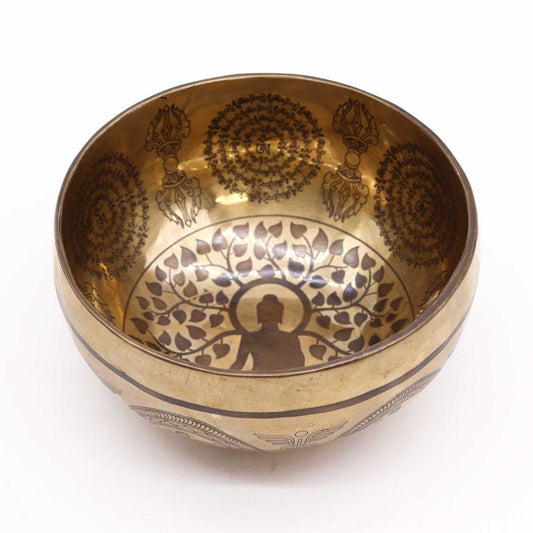 A brass bowl features intricate etched designs inside, depicting a seated figure under a tree with leaves. Circular patterns with symbols adorn the inner rim, and outer decorative accents are present.