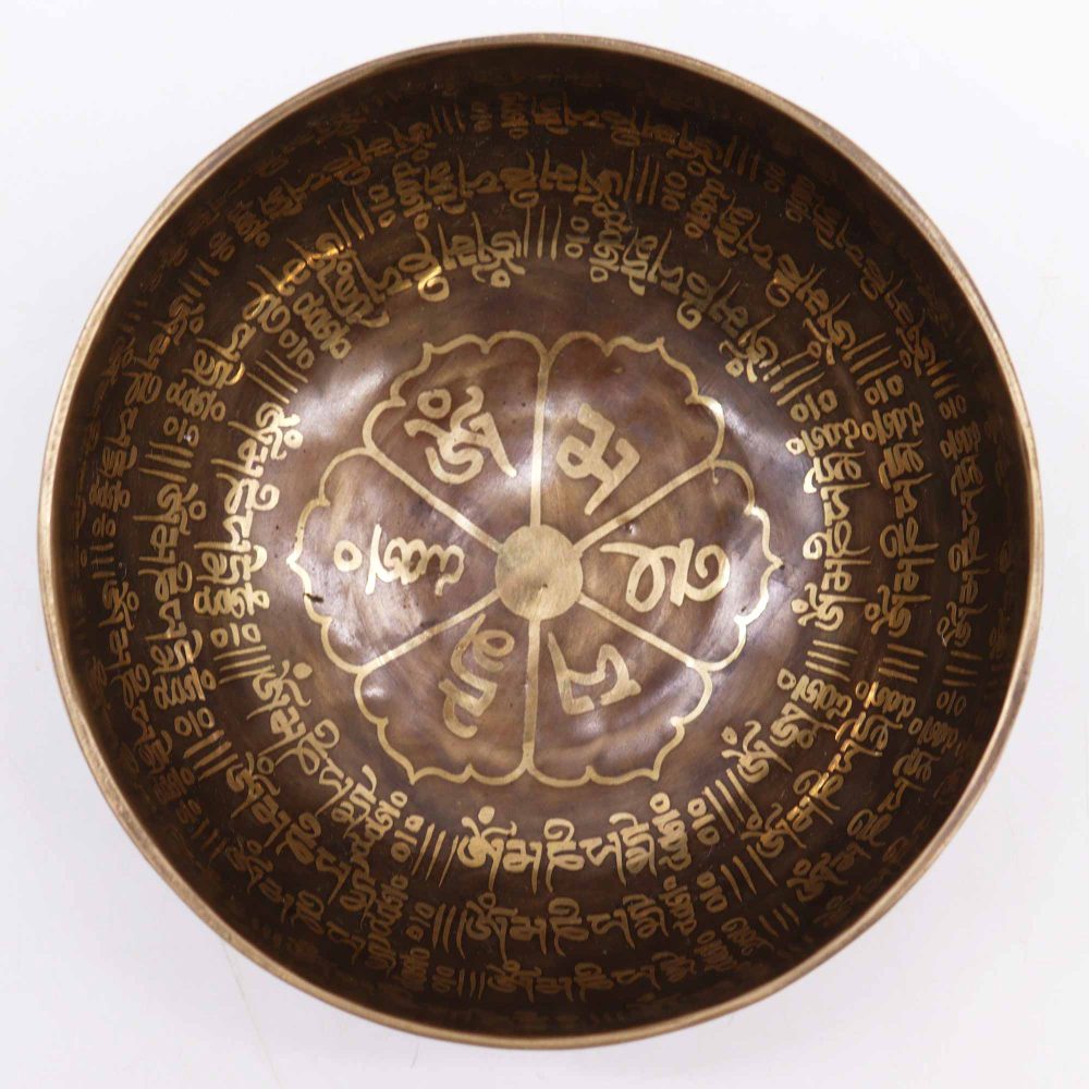 Bronze singing bowl, adorned with intricate gold Tibetan script, rests on a flat surface. The carvings form a circular pattern inside the bowl, creating an ornate and spiritual design.