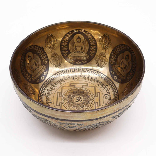 A decorative brass bowl features intricate engravings of seated figures and floral patterns inside, with Tibetan script encircling a central mandala design. The environment is minimal and well-lit.
