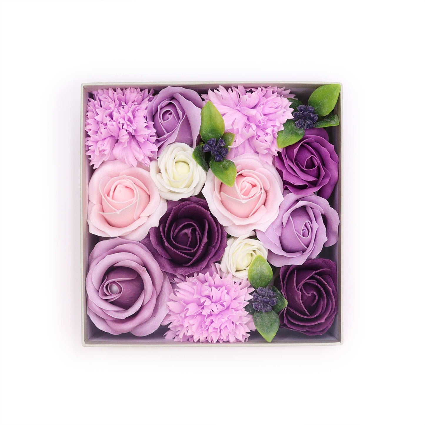 A square box contains an arrangement of soap roses and carnations in various shades of purple, pink, and white. The flowers are densely packed, creating a full, luxurious appearance. The context is a simple white background.