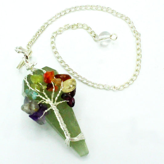 A pendulum, with a green cone-shaped crystal base, has a silver, tree-shaped wire around it holding colorful gems, suspended by a silver chain against a white surface.