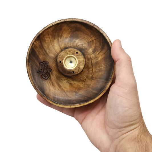 A hand holds a round, wooden disc with a central metal fitting and a carved Hamsa symbol, set against a plain white background.