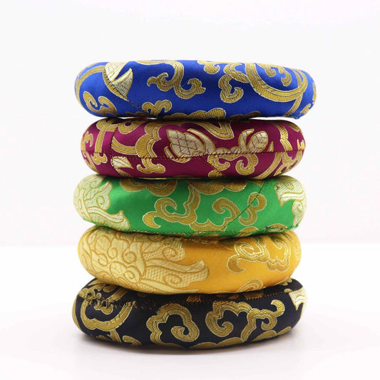Five ornate, ring-shaped cushions are stacked, each featuring a gold design on a different colored background. They rest on a white surface.