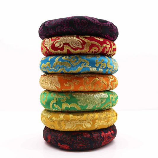 Eight round cushions, stacked vertically, are adorned with ornate, embroidered patterns in various colors. They rest on a white surface.