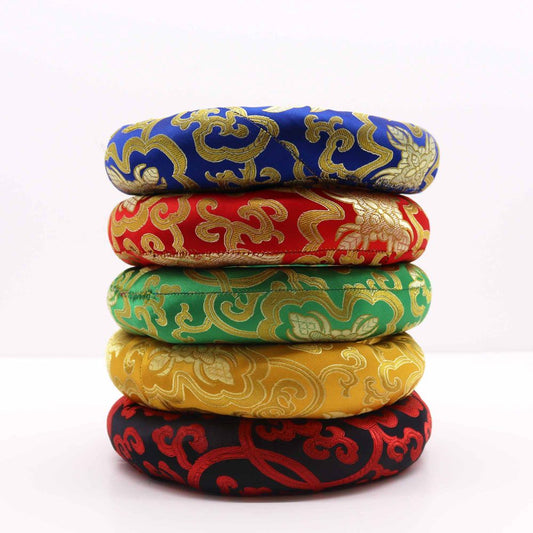 Five colorful, patterned meditation cushions are stacked on a white surface.