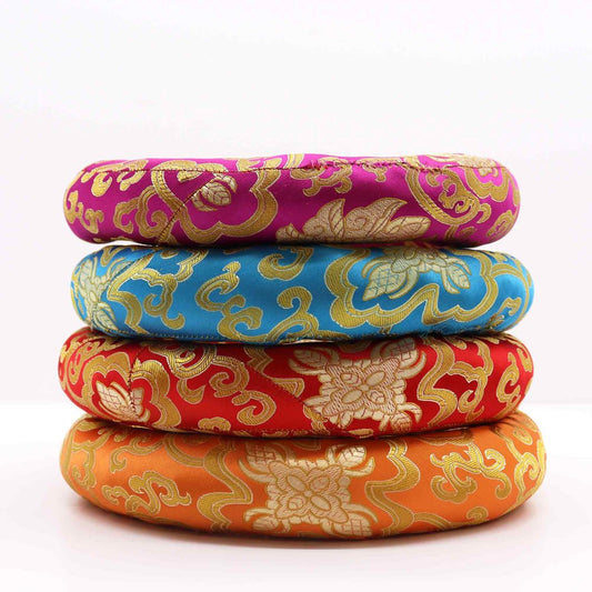 Four circular cushions, stacked, are adorned with ornate gold patterns on vibrant colored fabrics. The cushions rest on a white surface.