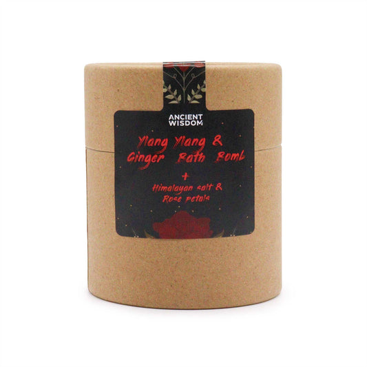 A cylindrical cardboard package labeled "Ancient Wisdom" contains "Ylang Ylang & Ginger Bath Bomb" with "Himalayan salt & Rose petals." The package sits against a plain white background.
