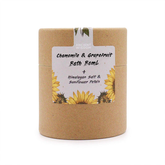 A cylindrical, brown container features a label with sunflowers, displaying: "ANCIENT WISDOM Chamomile & Grapefruit Bath Bomb + Himalayan Salt & Sunflower Petals," in a minimalist style.