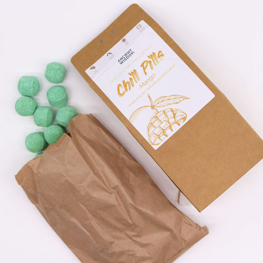 A brown paper bag labeled "Chill Pills - Mango" lies open, revealing several small, green, round tablets. Text: "Ancient Wisdom - Help Calm and Take a Dip with - Simply drop fizz and soak your stress away!"