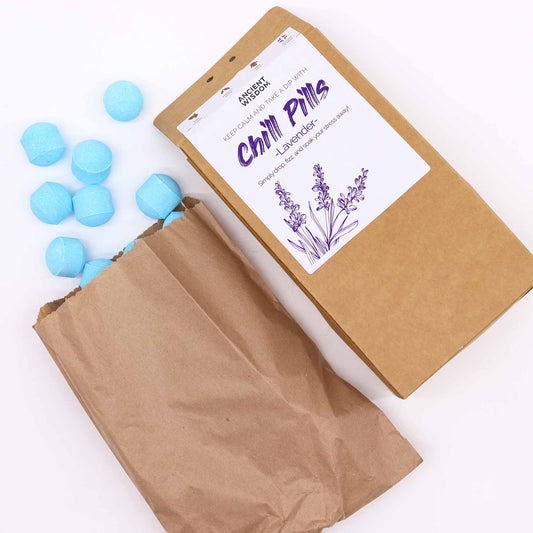 Brown paper bag spilling blue bath bombs, labeled "Chill Pills - Lavender," onto a surface beside a rectangular package featuring lavender illustrations. Text: "ANCIENT WISDOM, KEEP CALM AND TAKE A DIP."