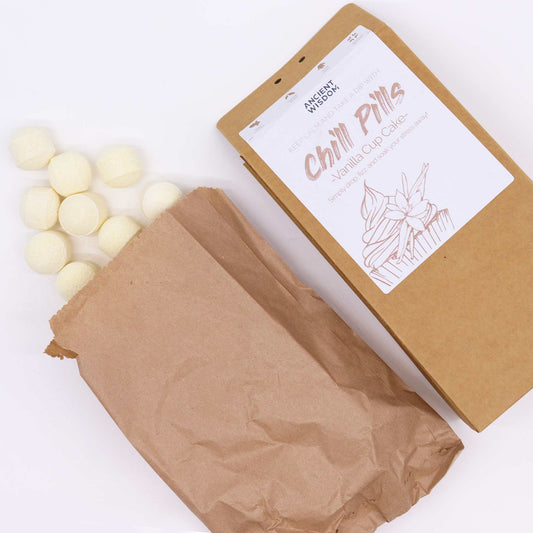 Brown paper bag spills white round items onto a surface. Nearby, a brown package labeled "Chill Pills - Vanilla Cup Cake" advises, "Simply drop a fizz & soak your stress away!"