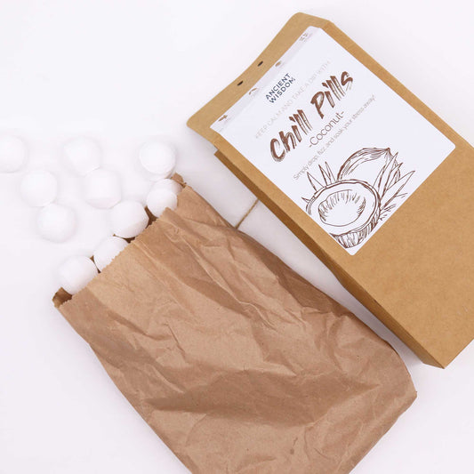 A brown paper package labeled "Chill Pills Coconut" by "Ancient Wisdom" displays white spherical objects spilling from an open paper bag, set on a white background. Transcription: "KEEP CALM AND TAKE A DIP WITH Chill Pills Coconut Simply drop in water and sink your stress away!"