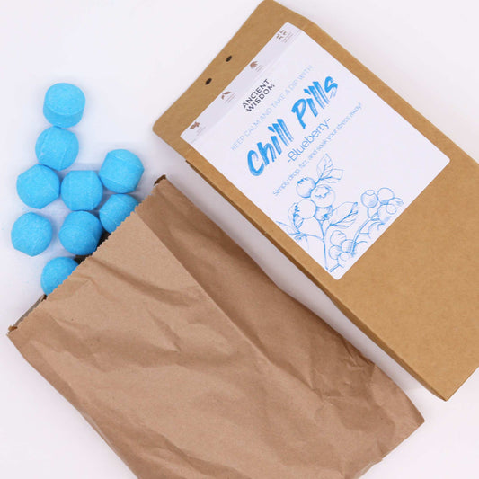 Bag of blue tablets spilling from a brown paper bag, next to a labeled box reading “Ancient Wisdom Chill Pills Blueberry” with a blueberry illustration.
