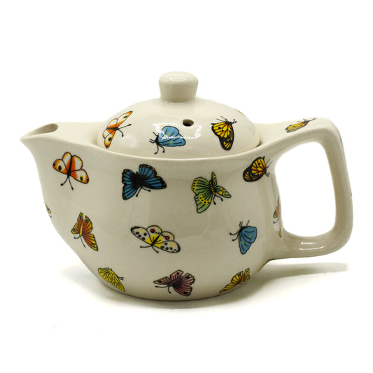 A ceramic teapot, adorned with colorful butterfly designs, sits on a white background. The teapot has a curved body, a handle, and a lid with a small hole.