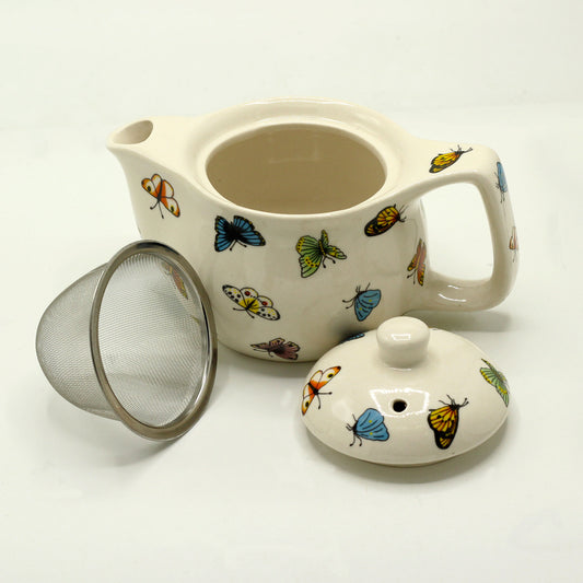 A butterfly-patterned teapot sits open, accompanied by its lid and a separate metal tea strainer, all on a white surface.