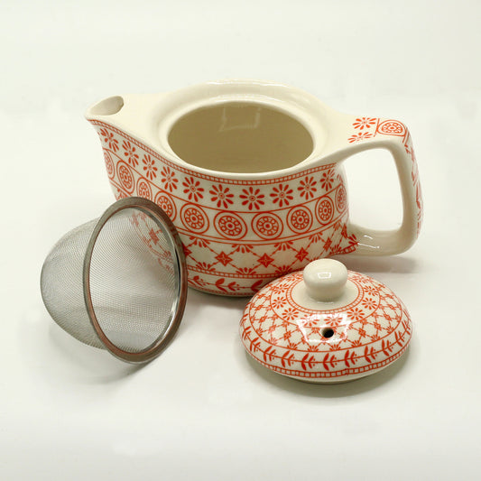 A patterned ceramic teapot sits open, accompanied by its lid and a separate metal tea infuser, all on a white surface.