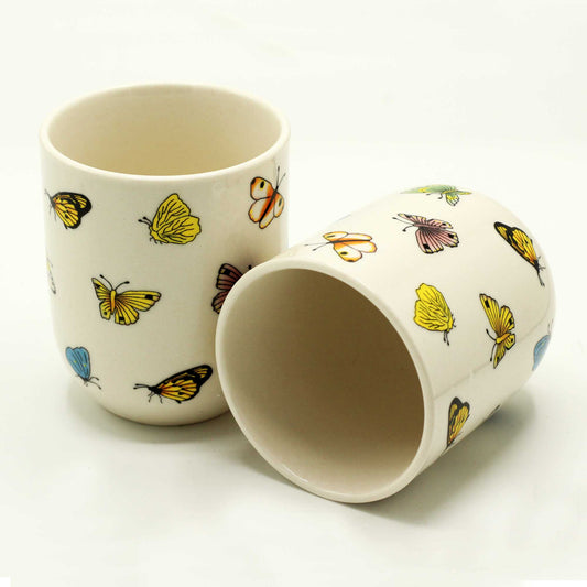 Two ceramic mugs, adorned with colorful butterfly patterns, sit on a white surface.