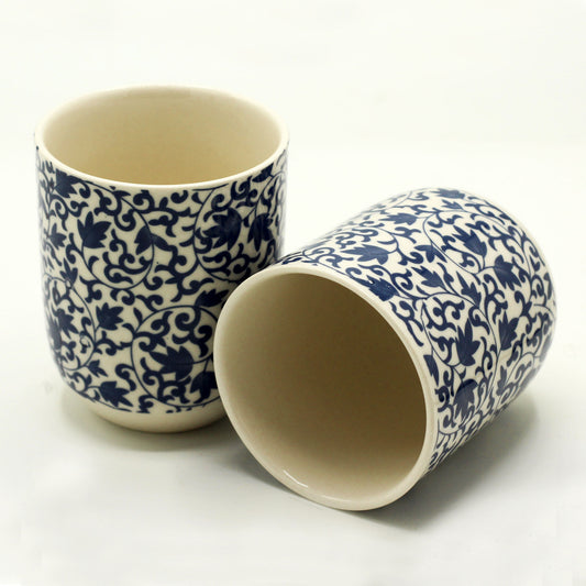 Two cylindrical ceramic cups, featuring a blue floral pattern, rest on a white surface.