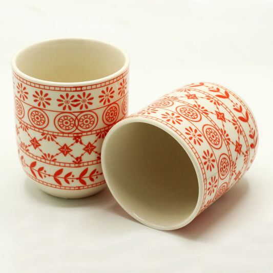 Two cylindrical mugs, adorned with an orange floral pattern, rest on a white surface.