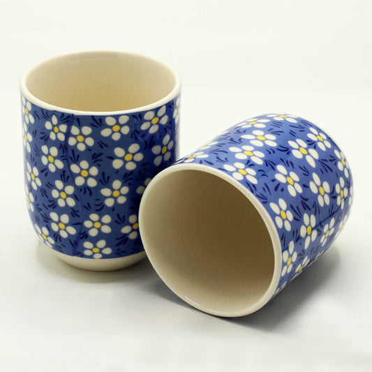 Two blue ceramic mugs, adorned with a small white flower pattern, rest on a white surface.