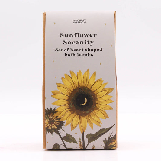 A box displays a sunflower illustration with a crescent moon in the center, surrounded by stars. Text reads: "ANCIENT WISDOM Sunflower Serenity Set of heart shaped bath bombs."