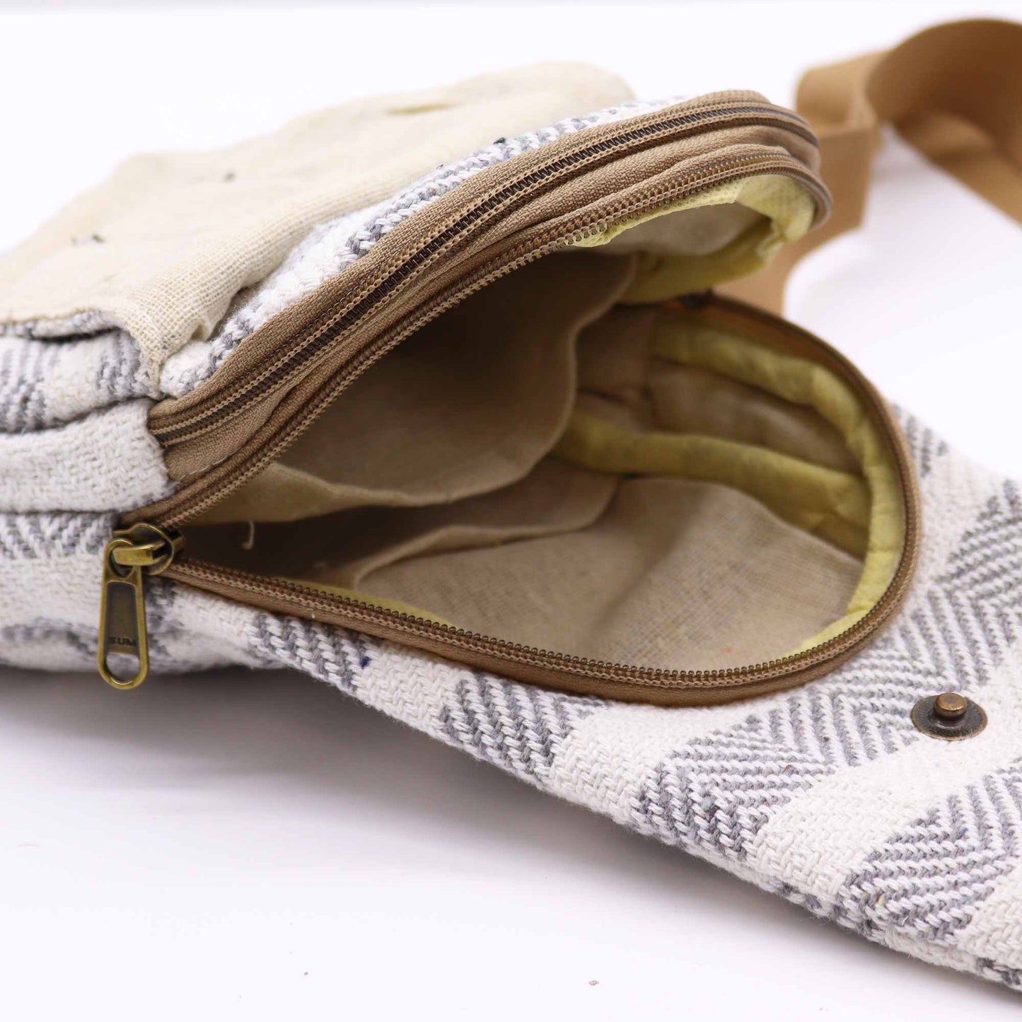 An open hemp bag, patterned with gray chevrons, reveals a yellow-lined interior and multiple compartments. A brown zipper is partially unzipped to reveal a small "SUM" engraving on the zipper pull. The bag sits on a white surface.