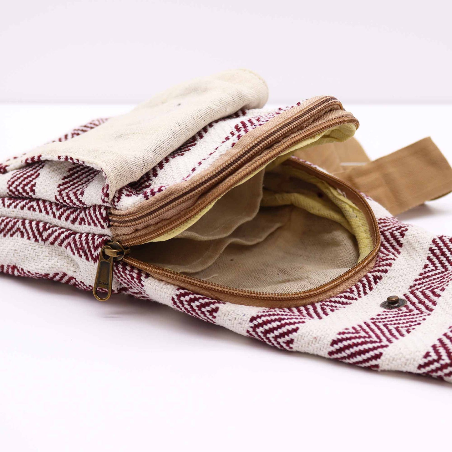 A partially unzipped bag rests on a white surface, its white fabric adorned with a burgundy chevron pattern. The bag’s tan interior and strap are visible through the open zipper.