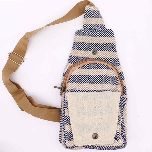 The triangular crossbody bag is oriented vertically. It is decorated with a zigzagging pattern of navy and tan and features brown straps, a zipped pocket, and a buttoned pocket on a plain white background.