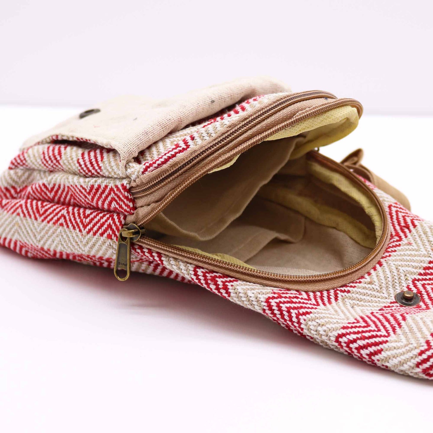 A textured, herringbone patterned bag with red and white colors sits open on a white surface. The zipper, reading “SUM”, is partially unzipped, revealing the bag’s beige interior.
