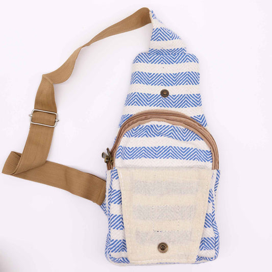 A sling bag with a brown strap and blue-and-white chevron pattern sits on a white surface. It features a top flap with a snap closure and a zippered front pocket.