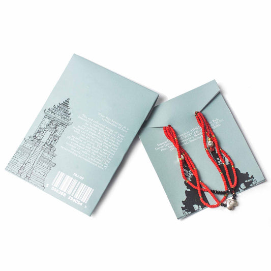 Red-beaded bracelets sit atop a light blue paper jewelry package. On the left, a similar package displays the text: "Wear this bracelet as a celebration of love," and "5 056368 334054 >".