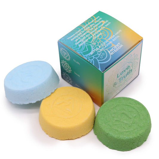 Three colorful bath bombs (blue, yellow, green) are placed beside a gradient-colored box. Text on the box reads: “These chakra stones… thought waves… enjoy a relaxing bath. Love & Truth. Ancient Wisdom. Truth, love.”