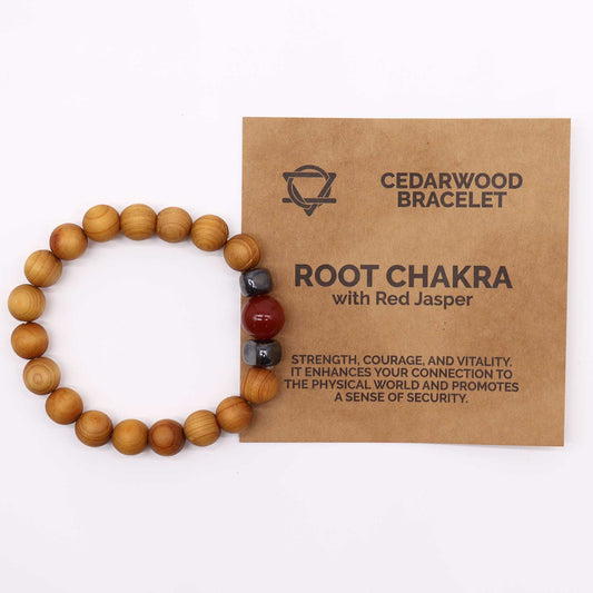 The cedarwood bracelet, with red jasper and dark stones, lies beside a brown card reading: "CEDARWOOD BRACELET," "ROOT CHAKRA," "STRENGTH, COURAGE, AND VITALITY. IT ENHANCES YOUR CONNECTION TO THE PHYSICAL WORLD AND PROMOTES A SENSE OF SECURITY."