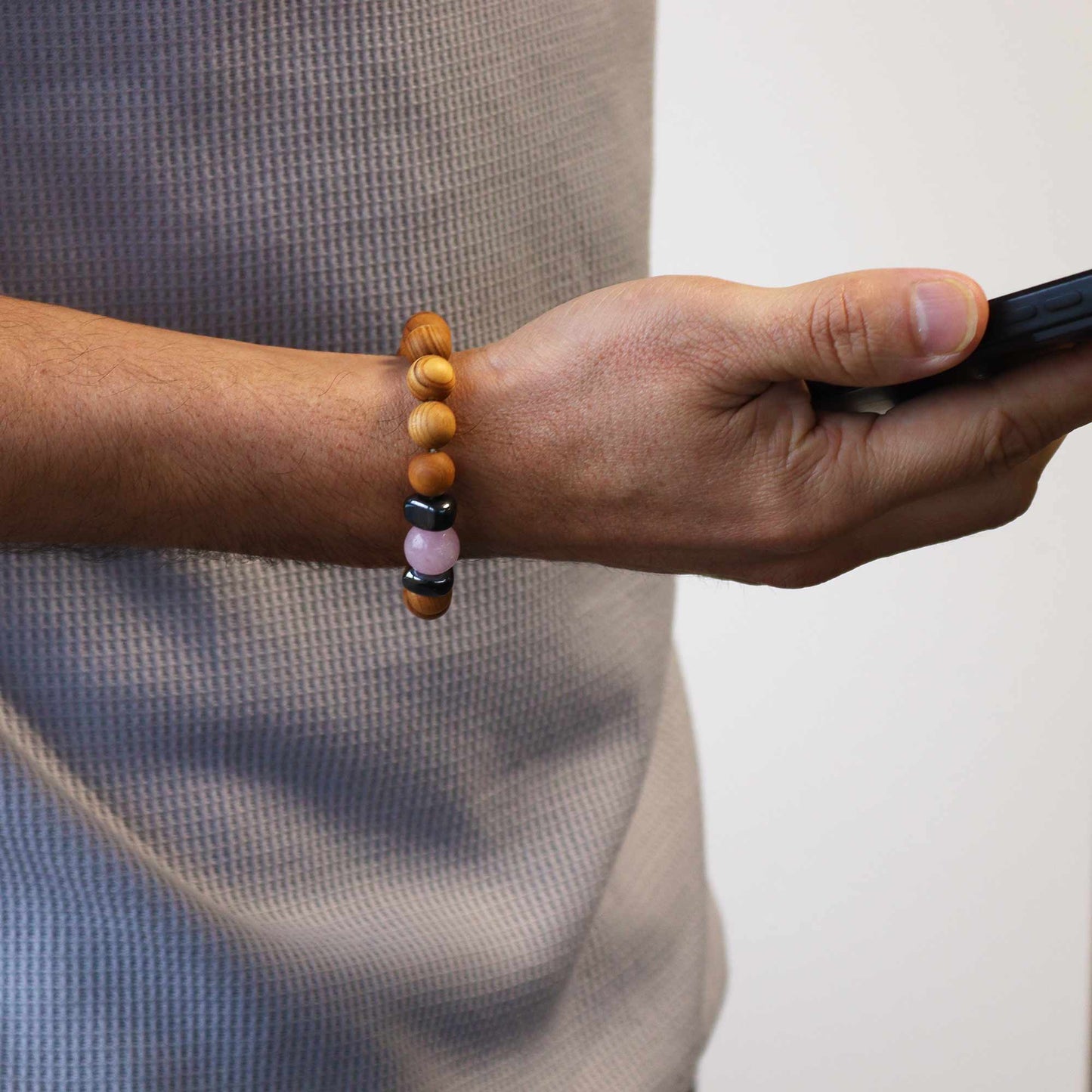 An arm with a beaded bracelet holds a smartphone. The beads are brown, pink, and black, in an indoor setting.