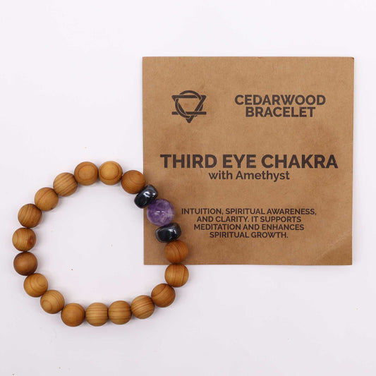 A bracelet made of wooden beads circles, interrupted by black and purple stones, set against a card. The card reads, "CEDARWOOD BRACELET THIRD EYE CHAKRA with Amethyst INTUITION, SPIRITUAL AWARENESS, AND CLARITY. IT SUPPORTS MEDITATION AND ENHANCES SPIRITUAL GROWTH."