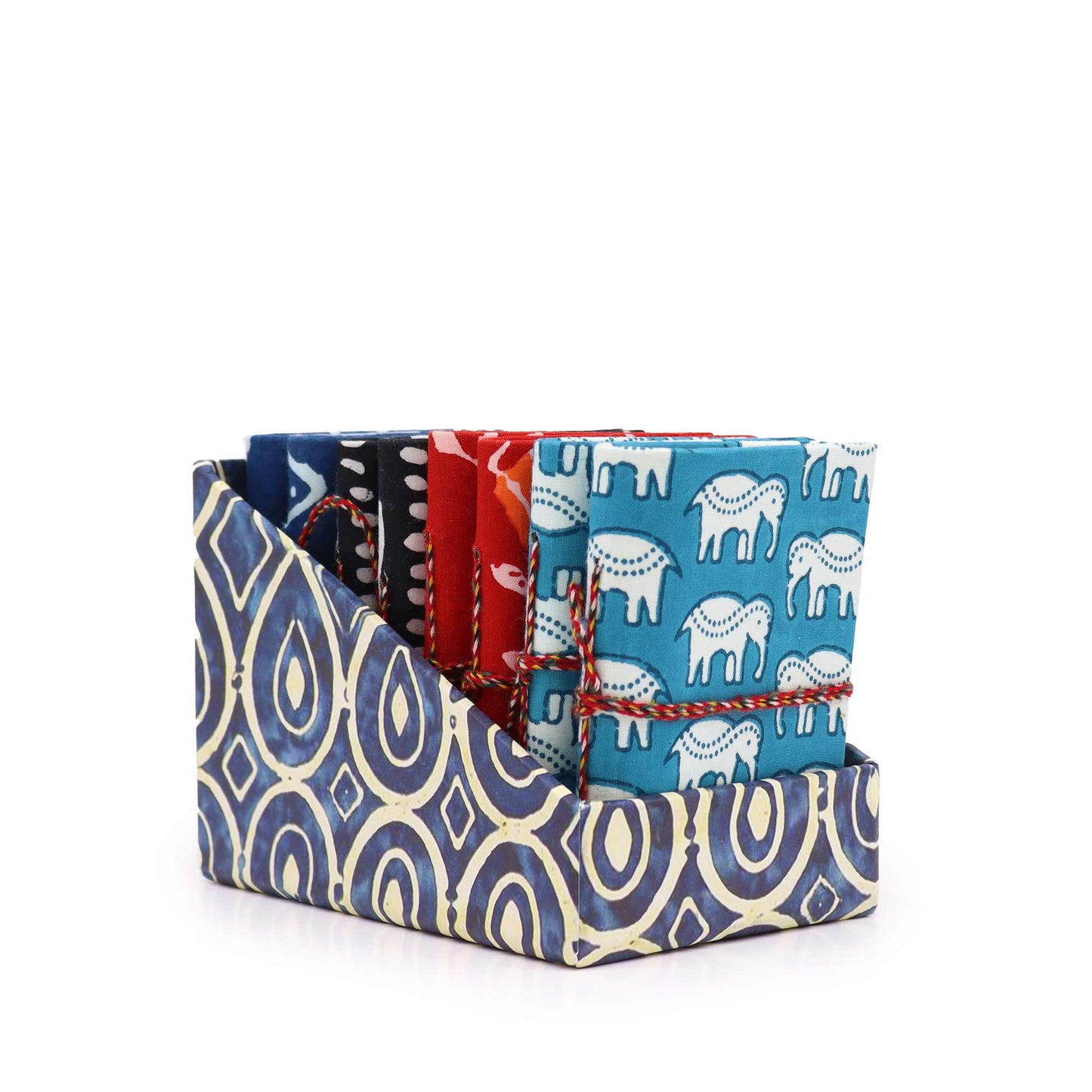 Colorful fabrics with various prints, including elephants and geometric patterns, are neatly folded and stacked. They are tied with string and arranged upright in a patterned fabric holder.