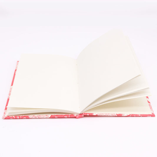 An open book displays blank cream-colored pages, resting on a flat surface. The cover is visible underneath, featuring a red and white pattern, suggesting a decorative or artistic design.