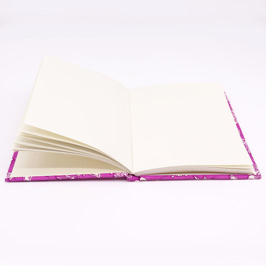 A purple-patterned hardcover notebook lies open with blank cream-colored pages, displayed on a plain white surface.