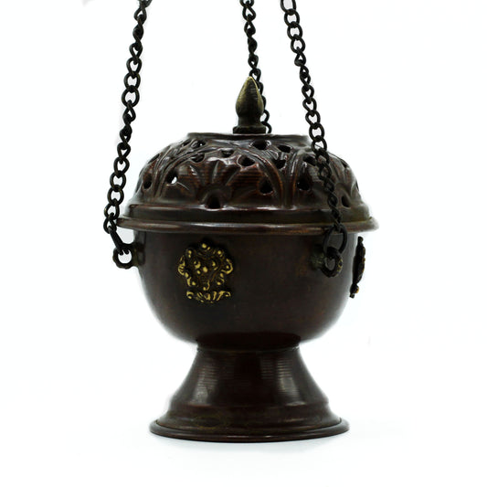 A bronze censer hangs on three chains, featuring decorative gold accents and an intricate, perforated lid, set against a plain white background.