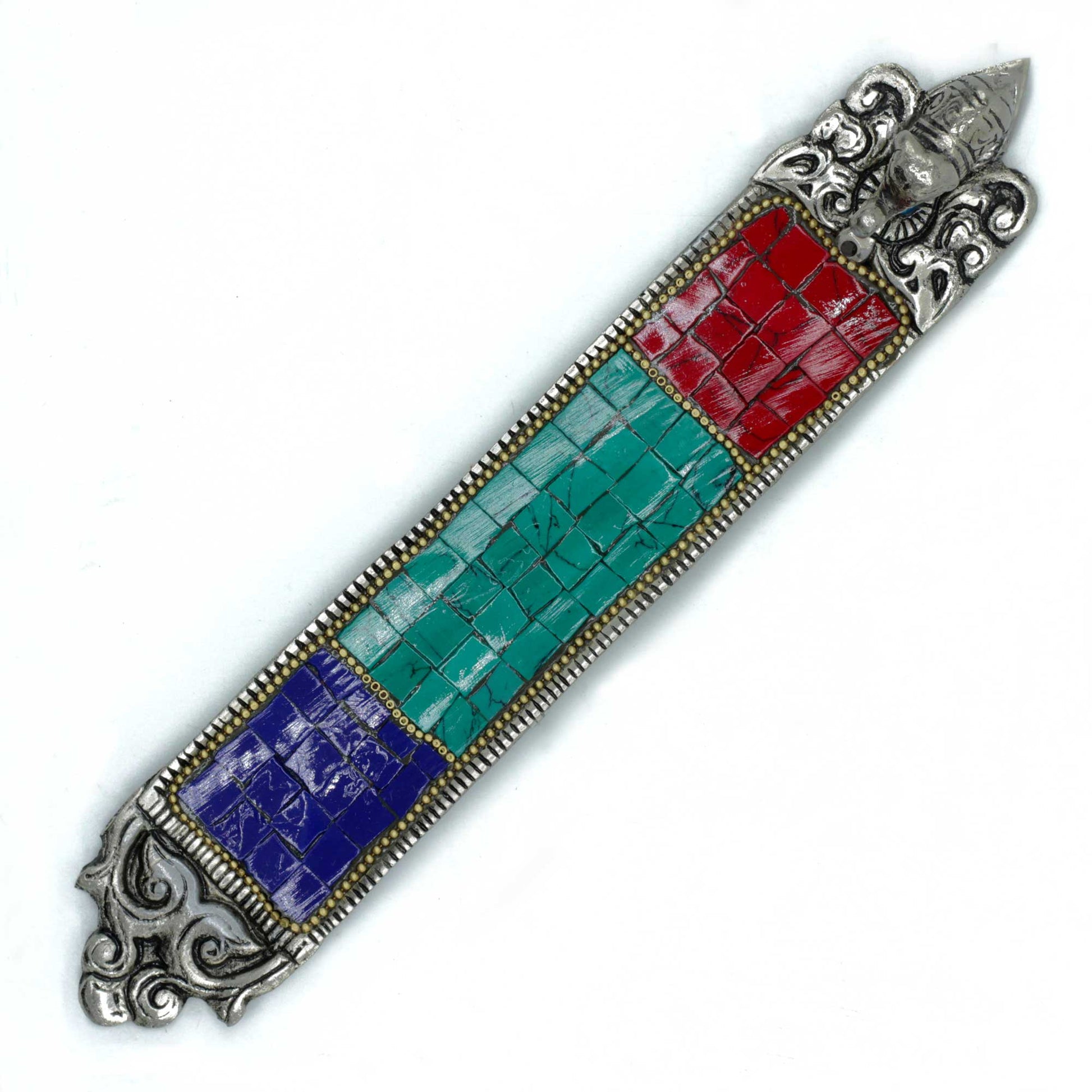 A rectangular, decorative piece features colorful tile patterns of red, green, and blue, bordered by silver accents. It is adorned with intricate, ornate designs and a small sculpted face at one end.
