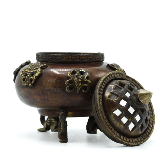 Bronze incense burner with intricate designs and a decorative lid featuring lattice patterns, sitting on three short legs. Set against a plain white background.